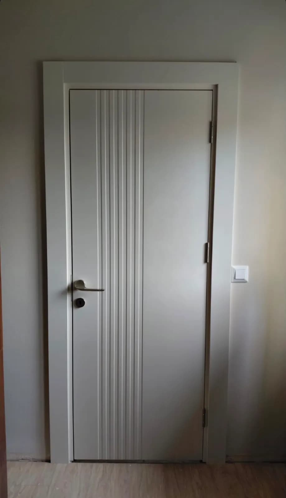 Beyaz dikey çizgi kabartmalı oda kapısı ve altın kol detayı